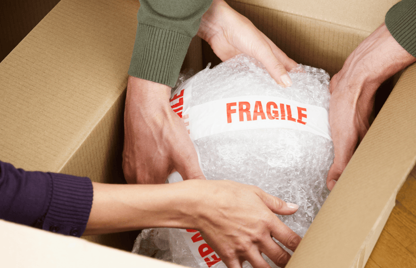 Two person are placing labelled fragile items in a box and used for a guide on packing tips for moving.